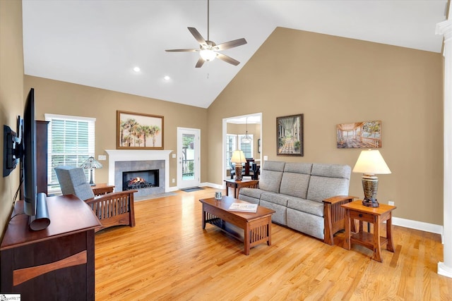 living area featuring light wood-style floors, a ceiling fan, a tiled fireplace, and high vaulted ceiling