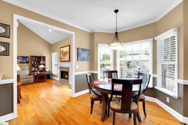 dining room with a fireplace, vaulted ceiling, baseboards, light wood-style floors, and ornamental molding