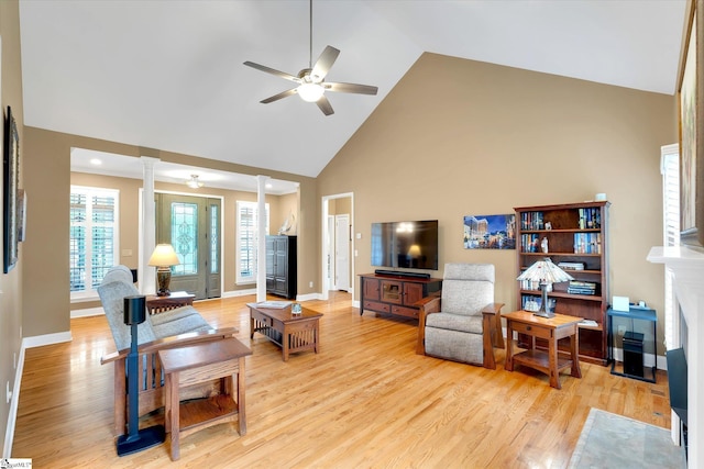 living area featuring light wood-style floors, baseboards, ceiling fan, high vaulted ceiling, and ornate columns