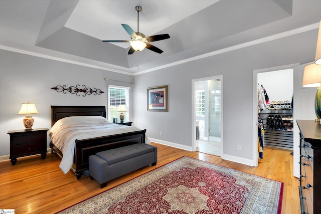 bedroom featuring ensuite bath, baseboards, light wood-type flooring, a tray ceiling, and a spacious closet