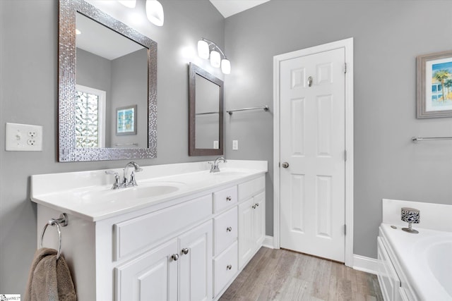 full bath with double vanity, a sink, a bath, and wood finished floors
