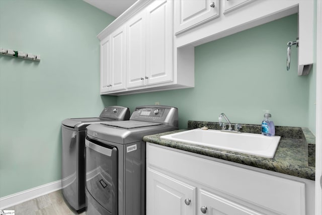 clothes washing area with cabinet space, a sink, baseboards, light wood-style flooring, and washer and clothes dryer