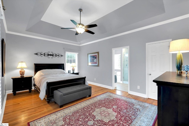 bedroom with crown molding, baseboards, light wood finished floors, connected bathroom, and a tray ceiling