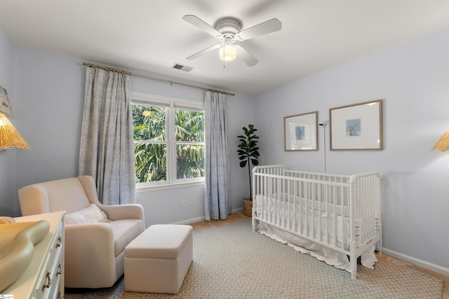 carpeted bedroom featuring a nursery area, baseboards, visible vents, and a ceiling fan