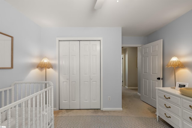 bedroom featuring a closet, baseboards, light colored carpet, a nursery area, and a ceiling fan
