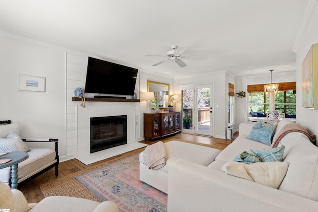 living area with crown molding, ceiling fan with notable chandelier, baseboards, a fireplace with flush hearth, and wood finished floors