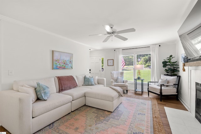 living area with ornamental molding, ceiling fan, a fireplace, and light wood-type flooring