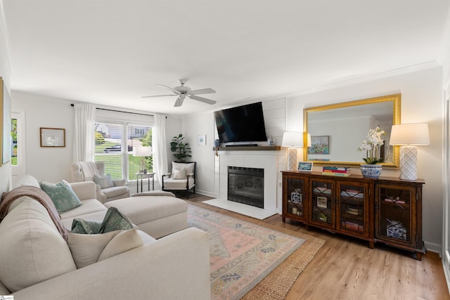 living area with a ceiling fan, a fireplace with flush hearth, ornamental molding, and wood finished floors