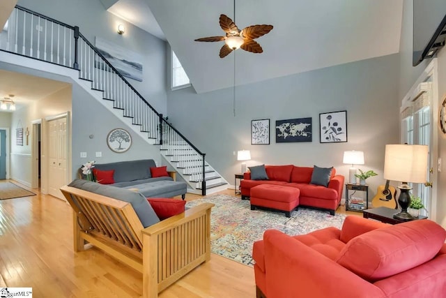 living area with stairs, ceiling fan, wood finished floors, and a towering ceiling