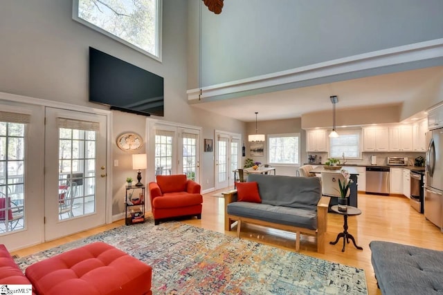 living room with light wood-type flooring, a towering ceiling, and french doors