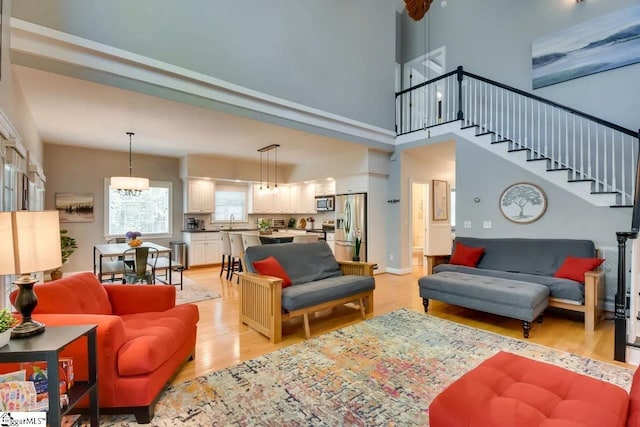 living area with stairs, a notable chandelier, light wood finished floors, and a towering ceiling