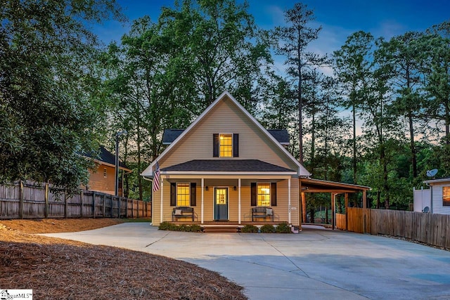 back of property at dusk with fence, covered porch, concrete driveway, and a carport