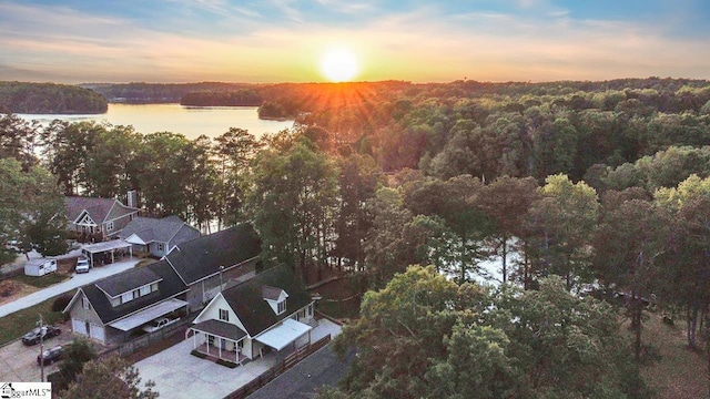 aerial view at dusk with a water view and a wooded view