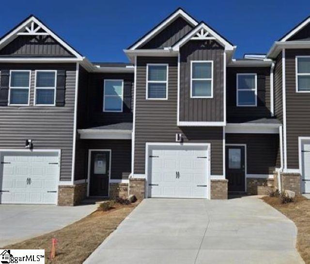 view of property with an attached garage, board and batten siding, concrete driveway, and stone siding