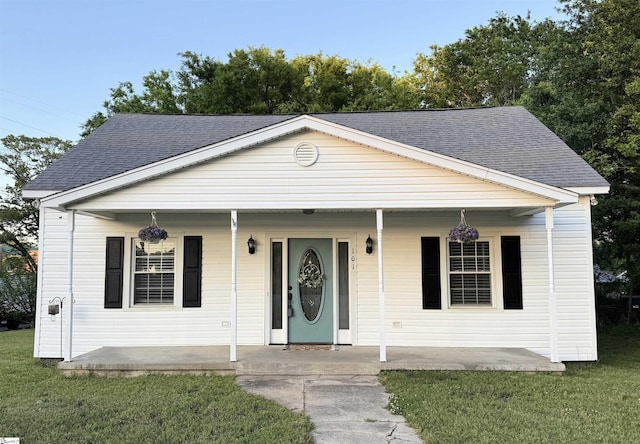 bungalow-style house featuring a shingled roof, a front lawn, and covered porch