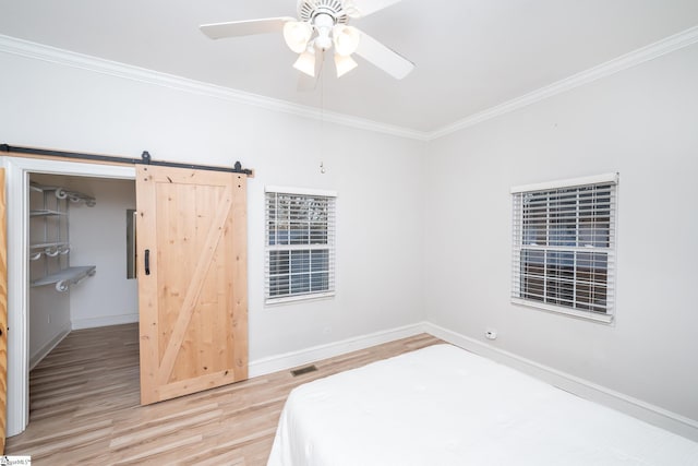 unfurnished bedroom featuring a ceiling fan, a barn door, baseboards, light wood-style floors, and ornamental molding