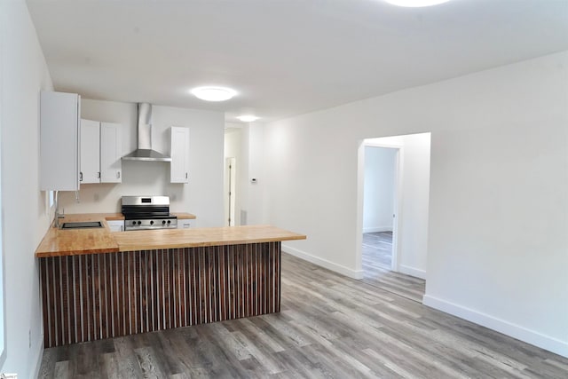 kitchen with stainless steel range with electric stovetop, light wood-style floors, wall chimney exhaust hood, a sink, and wood counters