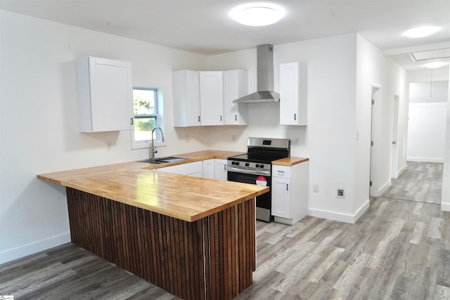 kitchen with a peninsula, wall chimney exhaust hood, a sink, wood counters, and stainless steel electric range oven