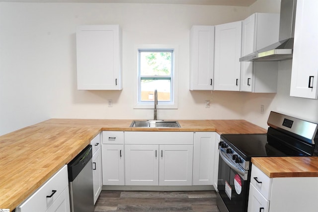 kitchen featuring appliances with stainless steel finishes, a sink, wood counters, wall chimney exhaust hood, and dark wood-type flooring