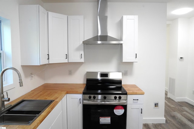 kitchen featuring visible vents, butcher block countertops, wall chimney exhaust hood, a sink, and stainless steel electric range oven