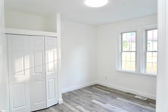 unfurnished bedroom with baseboards, visible vents, wood finished floors, and a closet