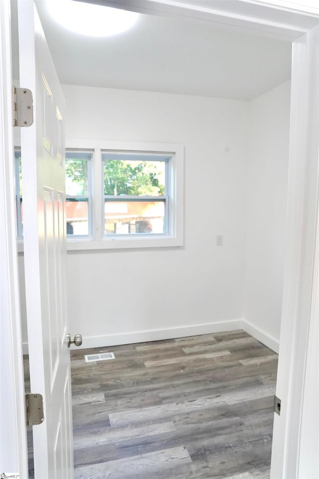 empty room featuring baseboards, visible vents, a healthy amount of sunlight, and wood finished floors