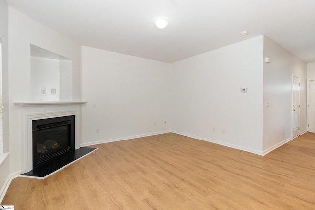 unfurnished living room featuring baseboards, a glass covered fireplace, and light wood-style flooring