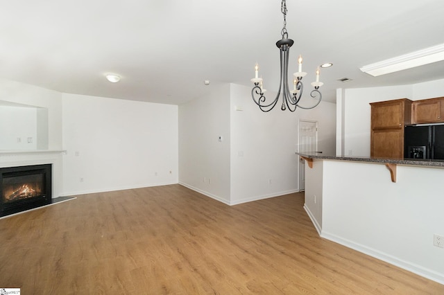 unfurnished living room featuring visible vents, a glass covered fireplace, baseboards, light wood finished floors, and a notable chandelier
