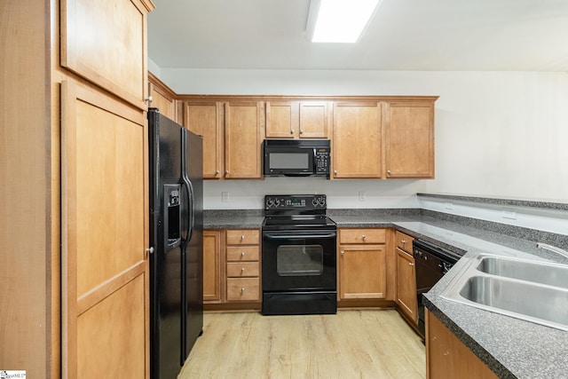 kitchen featuring a sink, dark countertops, black appliances, and light wood finished floors
