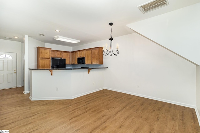 kitchen featuring a breakfast bar area, black appliances, light wood-style flooring, and visible vents