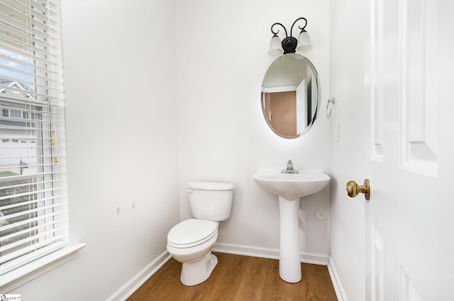 half bathroom featuring baseboards, a sink, wood finished floors, and toilet