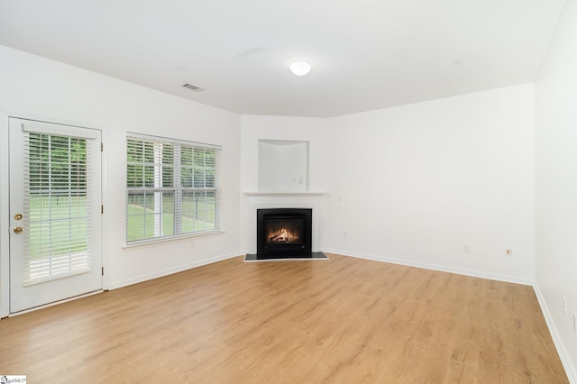 unfurnished living room with baseboards, a warm lit fireplace, visible vents, and light wood-style flooring