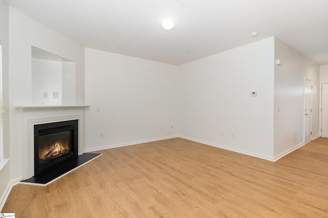 unfurnished living room with baseboards, a glass covered fireplace, and light wood-style floors