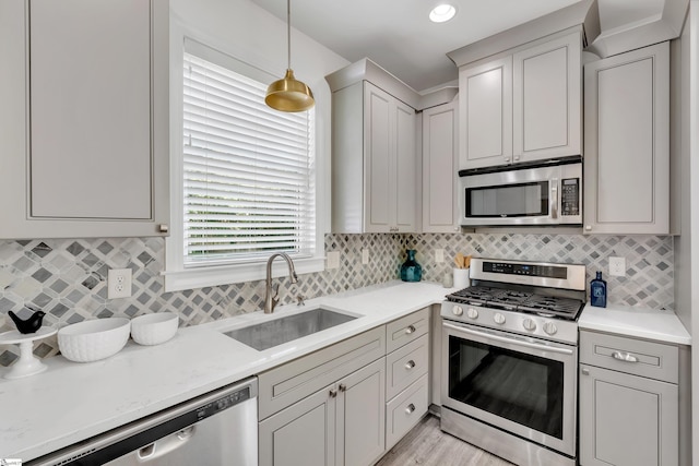 kitchen with gray cabinets, appliances with stainless steel finishes, tasteful backsplash, hanging light fixtures, and a sink