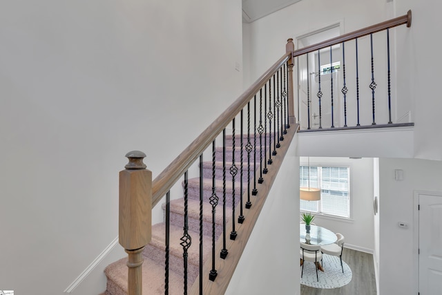 stairway with baseboards, wood finished floors, and a towering ceiling