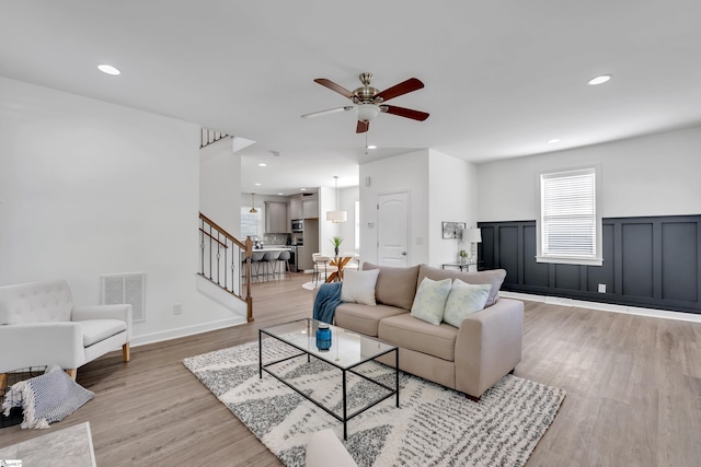 living area featuring ceiling fan, visible vents, wainscoting, stairway, and light wood-style flooring