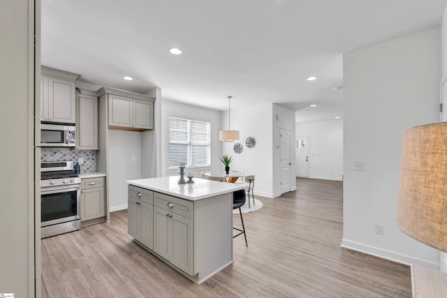 kitchen featuring stainless steel appliances, a breakfast bar, gray cabinets, and light wood-type flooring