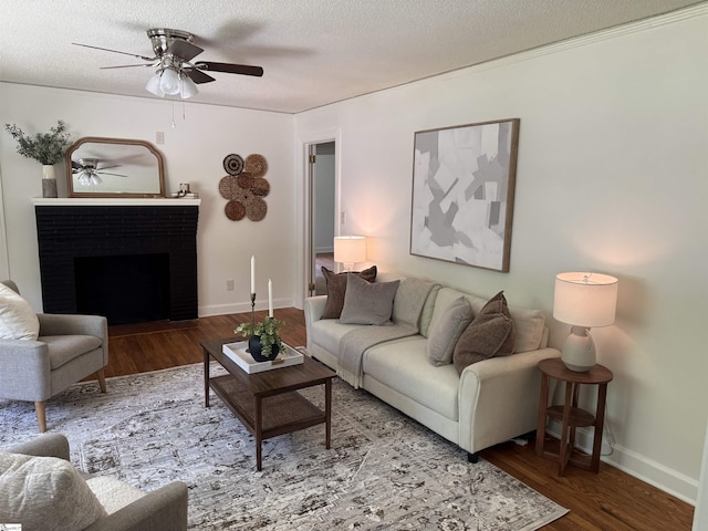 living room with a ceiling fan, a textured ceiling, a brick fireplace, and wood finished floors