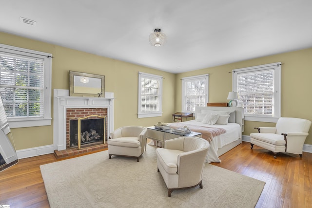 bedroom with baseboards, multiple windows, a fireplace, and hardwood / wood-style flooring