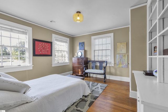 bedroom featuring baseboards, ornamental molding, wood finished floors, and visible vents