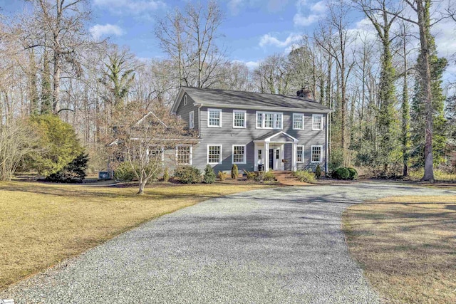 colonial inspired home featuring covered porch, a chimney, driveway, and a front yard