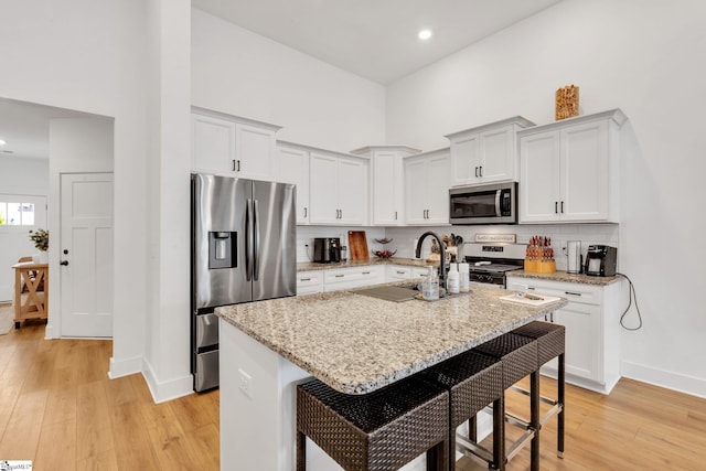 kitchen featuring decorative backsplash, baseboards, a kitchen bar, light wood-type flooring, and appliances with stainless steel finishes