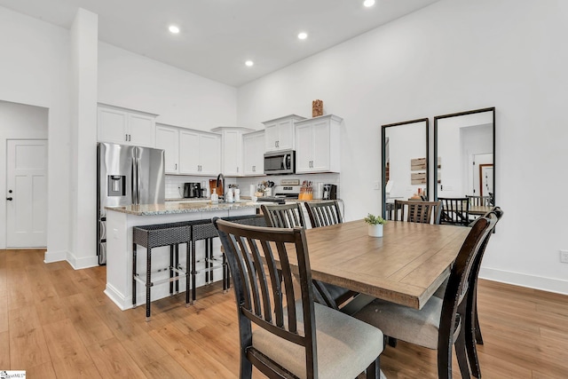 dining room featuring recessed lighting, baseboards, light wood finished floors, and a towering ceiling