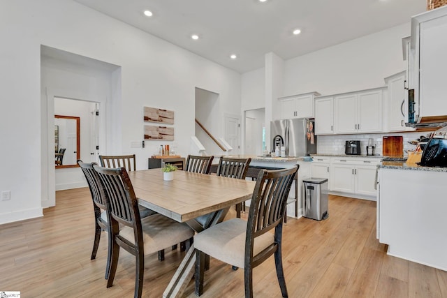 dining area with baseboards, recessed lighting, light wood-style flooring, and a towering ceiling
