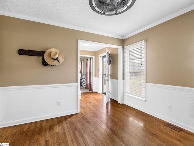 unfurnished room with a textured ceiling, ornamental molding, wood finished floors, and visible vents