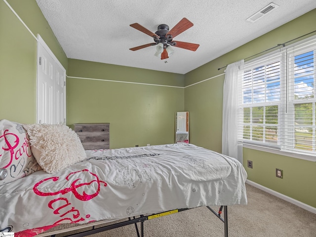 bedroom featuring a ceiling fan, a textured ceiling, visible vents, baseboards, and carpet floors