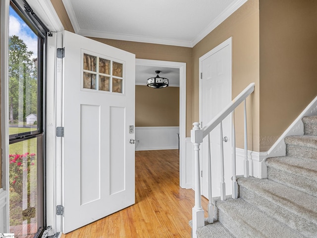 entrance foyer with crown molding, stairway, and light wood-style floors