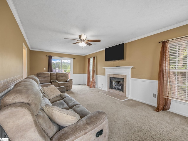 living room featuring ornamental molding, carpet flooring, a fireplace, a wainscoted wall, and a ceiling fan