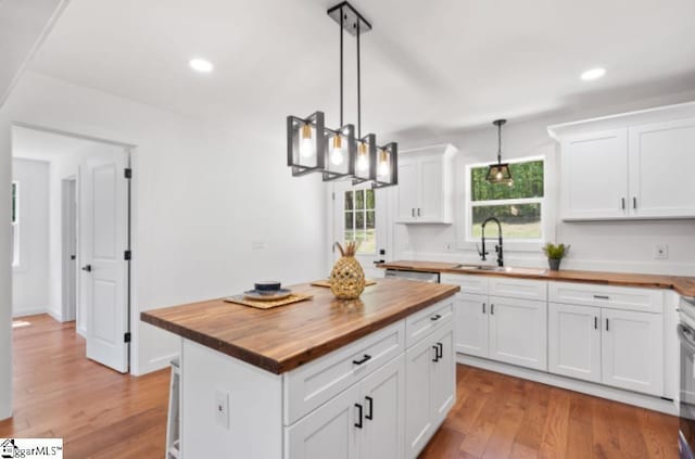 kitchen with light wood-type flooring, a sink, wood counters, and white cabinetry