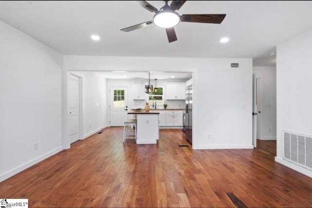 kitchen with dark countertops, a ceiling fan, white cabinetry, a kitchen bar, and visible vents